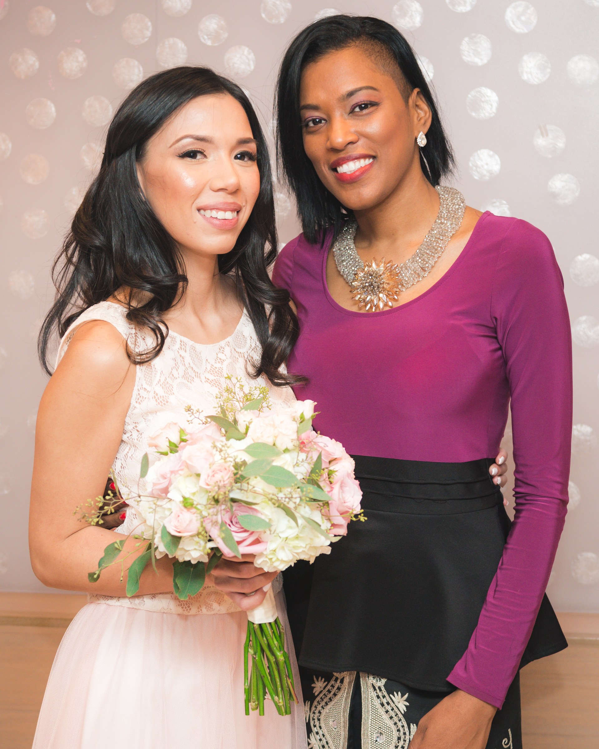 Bride posing with a guest against a soft pink backdrop
