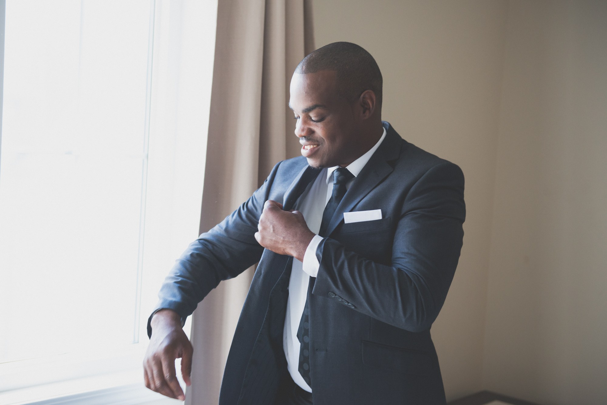 Groom fastening his jacket in soft window light