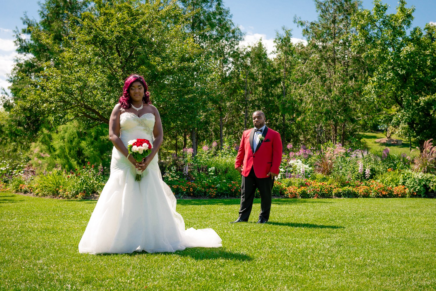 Couple in red and white wedding attire in a sunlit garden